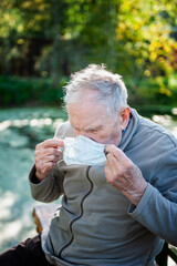 An old 87-year-old man puts on a mask while sitting outside. Protection against viruses and...