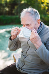 An old 87-year-old man puts on a mask while sitting outside. Protection against viruses and...