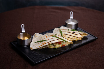 Tortillas with meat filling and sauce on a black plate