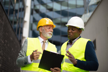   Mature engineer discussing the structure of the building with architects colleague at construction site. Reading document.