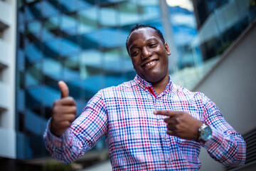 Smiling business man outside, gesturing with hand. Showing on thumb up.