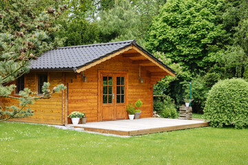 Wooden hut in spring. Garden shed for vacation. Nice garden in Germany. Well-kept garden with freshly cut green grass and potted plants  - obrazy, fototapety, plakaty