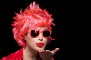 Stylish young woman wearing trendy modern sunglasses and red wig blowing across the palm of her...