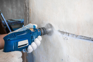drills a hole for an electrical outlet in a concrete brick wall.  Construction worker man with...