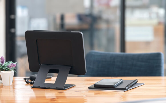 Rear view of tablet with stand holder on wooden table in modern office room.