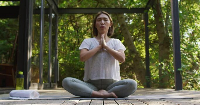 Asian woman meditating and sitting on yoga mat in garden