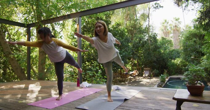 Asian mother and daughter practicing yoga outdoors in garden