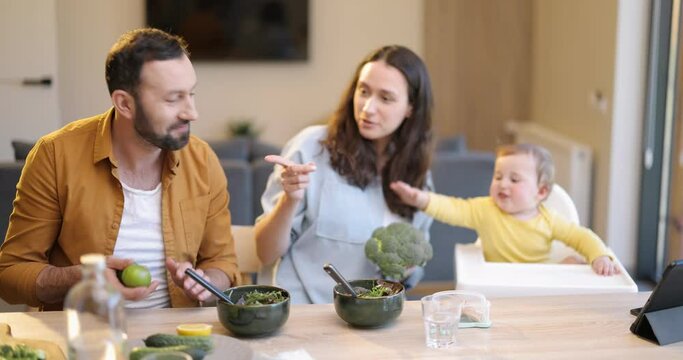 Family having fun with their baby son during a lunch time at home. Man juggling lemons. Concept of healthy vegan eating and happy parenting