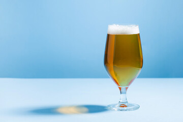 Refreshing beer in a glass on a blue background with a hard shadow. Copy space.