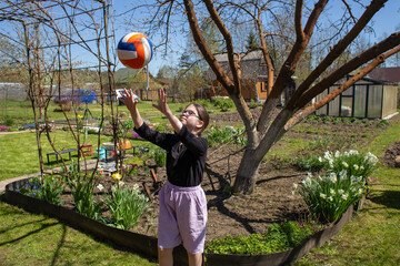 Teenage girl playing with a volleyball ball in a blooming garden in early spring