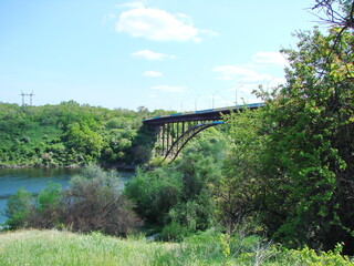 View from the thickets of the Dnieper forest on the arched bridge against the blue barely cloudy sky.