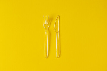 Transparent plastic fork and knife on yellow background. Minimalist disposable tableware. Concept meal and food delivery or takeaway