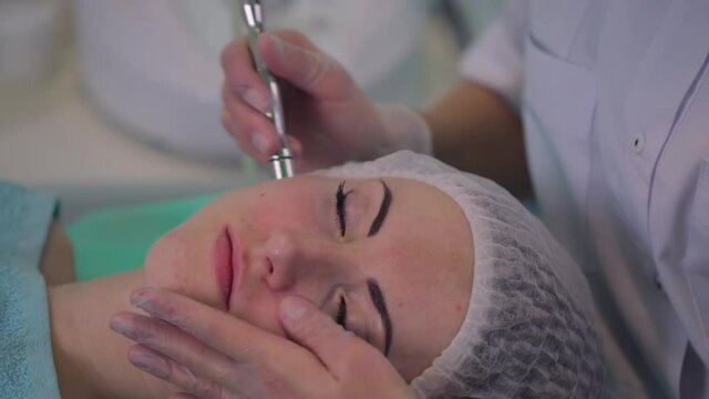 Cosmetological procedure microdermabrasion for a girl with problem skin. The beautician makes a treatment procedure to the patient.