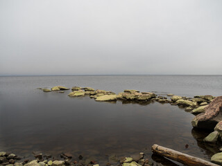 A spit of stones along the coast line. Greenish stones. Rocks with moss. The horizon line in the distance. Cloudy weather. Beautiful natural landscape.