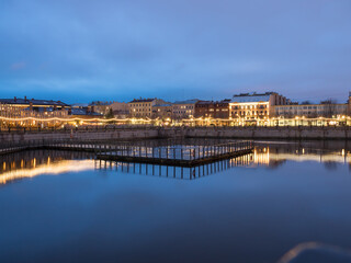Obraz premium Night view of the city from the side of the river: ancient architectural buildings, garlands, alleys and paths. There is a pier for boats on the river. Beautiful city in colored lights