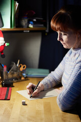 Portrait of caucasian adult woman is writing at the table at home. High resolution photos