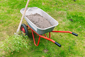 Garden trolley with soil on the lawn. Metal construction trolley for work in the garden. Gardener's tool with wheels for transporting earth, weeds, sand and soil. Gardening and agriculture