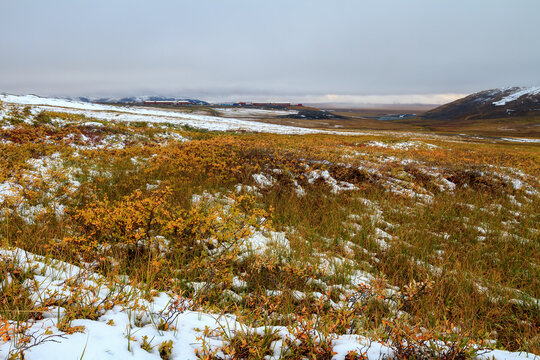View of the tundra and hills. In the distance, there is a working village of miners near a gold ore deposit. August, cold snowy summer in the Arctic. Mayskoye mine, Chukotka, Siberia, Far North Russia