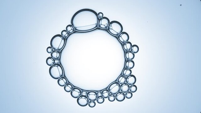 Bubble cluster of five small transparent bubbles joins to big transparent bubble with small ones spreading on its surface against cyan background | Shot of skincare gel ingredients for its commercial
