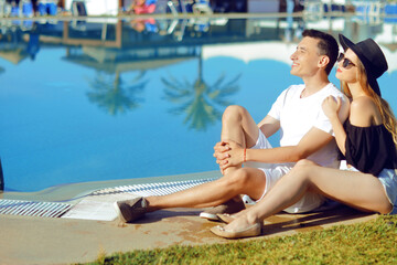  A sunny day, a man and a girl enjoy the rest. Travel. Against the background of palm trees and houses. Couple at the hotel with a pool. The concept of relaxation and travel. Kiss