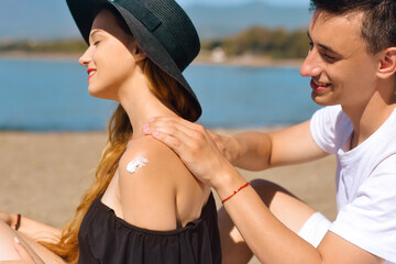 Fototapeta na wymiar Suncare couple on a summer beach vacation have good skincare with high spf sunblock. Couple applying suncream. Handsome man putting sun tan lotion on his girlfriend at the beach. Vacation, tourism.