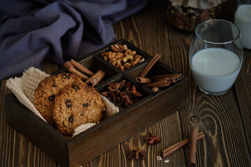 Fototapeta premium Delicious and flavorful oatmeal cookies with nuts, raisins and spices with a cup of milk on old wooden table
