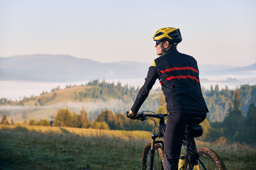 Close up male cyclist in cycling suit riding bike with hills on background. Man bicyclist wearing...