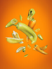 Green peppers flying and falling down isolated on vibrant orange background. Creative food concept. Spicy vegetable cuisine. Healthy and organic diet.