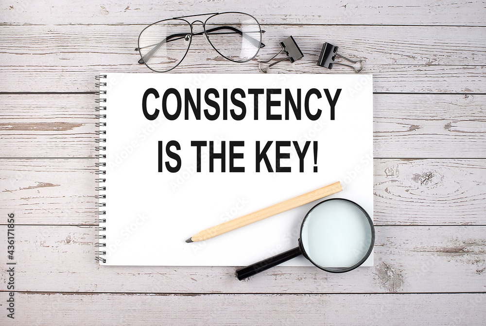 Poster notebook with text consistency is the key on the wooden table with pen, magnifier and glasses