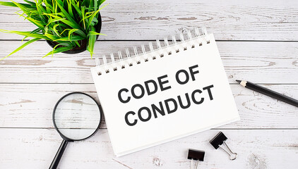 CODE OF CONDUCT text concept write on notebook with office tools on the wooden background