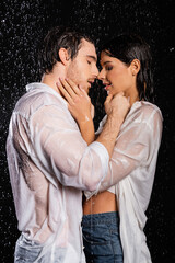wet passionate couple holding hands near faces in rain drops on black background