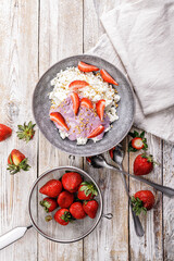 Top view fresh juicy ripe strawberries and farmers delicious cottage cheese with ripe fruit pieces. Organic food on your table. Delicious and healthy breakfast ideas. Vertical shot. Copy space
