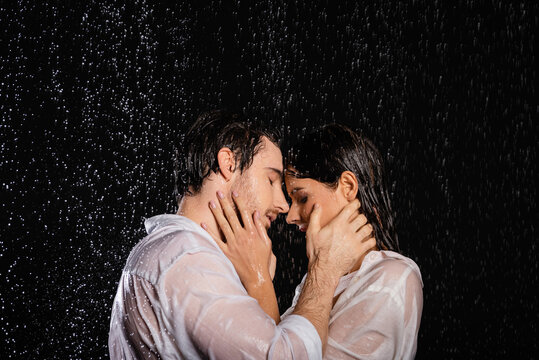 wet passionate romantic couple holding hands near faces in rain drops on black background