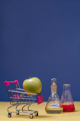 a green apple in a mini-cart next to there are flasks with nitrates. Eco products concept in...