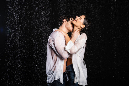 romantic boyfriend embracing with sexy girlfriend in wet clothes in rain drops on black background