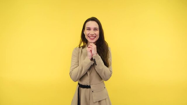 Joyful woman with braces on her teeth and in causal clothes stands on a yellow background and emotionally happy looking at the camera