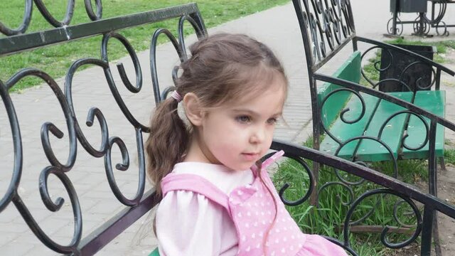 girl on a park bench eating a donut with yellow frosting. happy childhood, outdoor recreation, walks. Cheerful Child Sitting on Park Bench