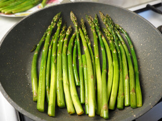 green young thin asparagus fried in a gray round frying pan side view. cooking at home in the kitchen