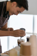 Young Caucasian barista man smiling and happy as enjoy decorating creamy foam of cold drinks in...