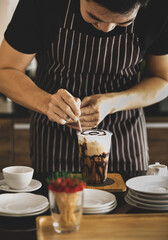 Barista carefully decorating creamy foam of iced coffee by using toothpick to draw chocolate patterns onto it like spider net to make it look more attractive to be drunk