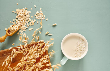 Oat milk in a glass and mug on a blue background. Flakes and ears for oatmeal and granola on a...