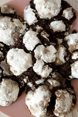 Homemade Chocolate Crinkle Cookies on a pink plate on a white wooden surface, top view. Flat lay, overhead, from above. Close-up.