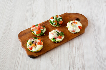 Homemade Egg White Breakfast Cups with Spinach and Tomato on a rustic wooden board, side view.