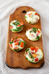 Homemade Egg White Breakfast Cups with Spinach and Tomato on a rustic wooden board, side view.