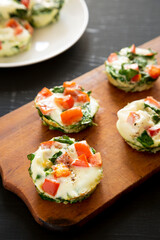 Homemade Egg White Breakfast Cups with Spinach and Tomato on a rustic wooden board on a black background, side view.