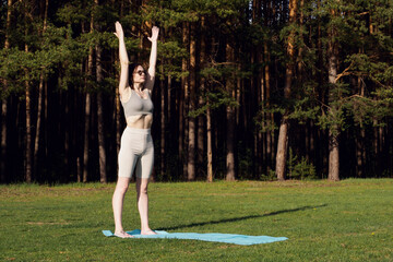 A young slender girl does yoga, performs asanas on a mat, in nature. Outdoor sports, healthy...