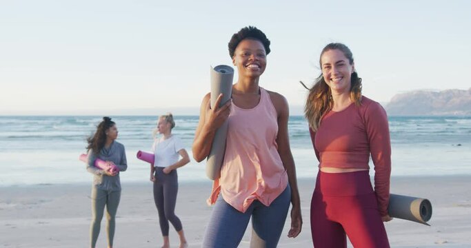 Group of diverse female friends holding yoga mats at the beach