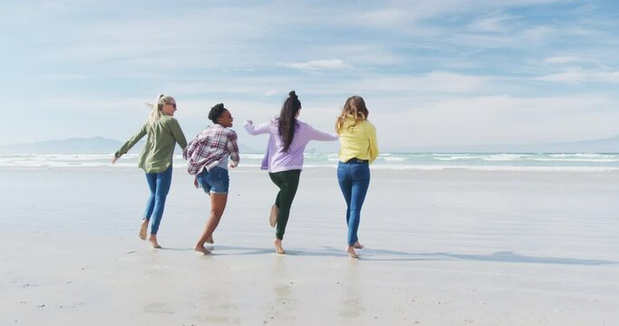 Happy group of diverse female friends having fun, running at the beach