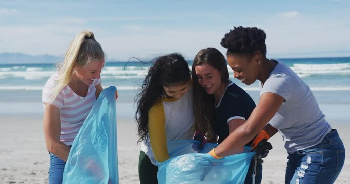 Diverse group of female friends putting rubbish in refuse sacks at the beach