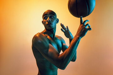 Handsome african-american male basketball player training in neon light on orange background.